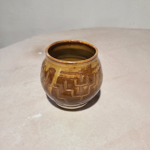 Ceramic bowl with angular, nested carvings that causes the golden brown glaze to break and flow.