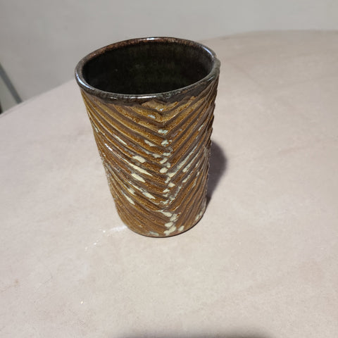 The carving on this ceramic cup guides and gathers the flowing, sandy glaze on the exterior, a stark contrast to the black glossy glaze on the interior.