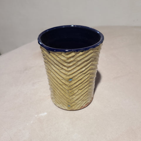 The carving on this ceramic cup guides and gathers the flowing, sandy glaze on the exterior, a stark contrast to the navy blue glossy glaze on the interior.