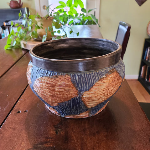 Ceramic bowl with a wide curved shoulder narrowing to a strong lip. Surface features carved texture and alternating colors between reddish-orange and blue-green.
