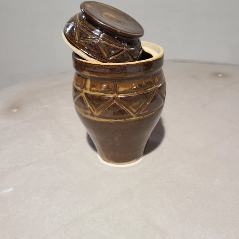 The luscious curves of this ceramic lidded vase are contrasted with the sharp, linear carvings that gather and guide the flowing golden-brown glaze.