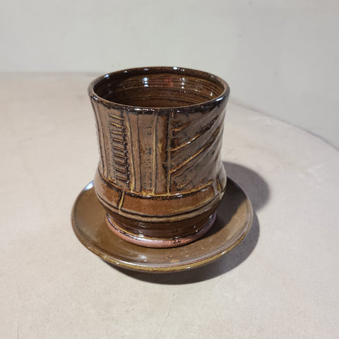 Carved ceramic planter set with deep brown glaze that flows over the combination of vertical and horizontal lines carved into this side of the vase..